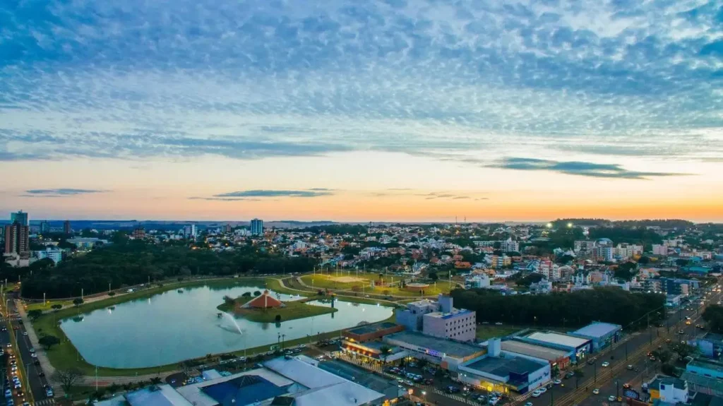 Imagem da vista aérea do Parque Ecológico Diva Paim Barth, em Toledo, mostra lago, casas e prédios ao fundo cercados por vegetação para ilustrar matéria sobre as cidades mais desenvolvidas no Brasil