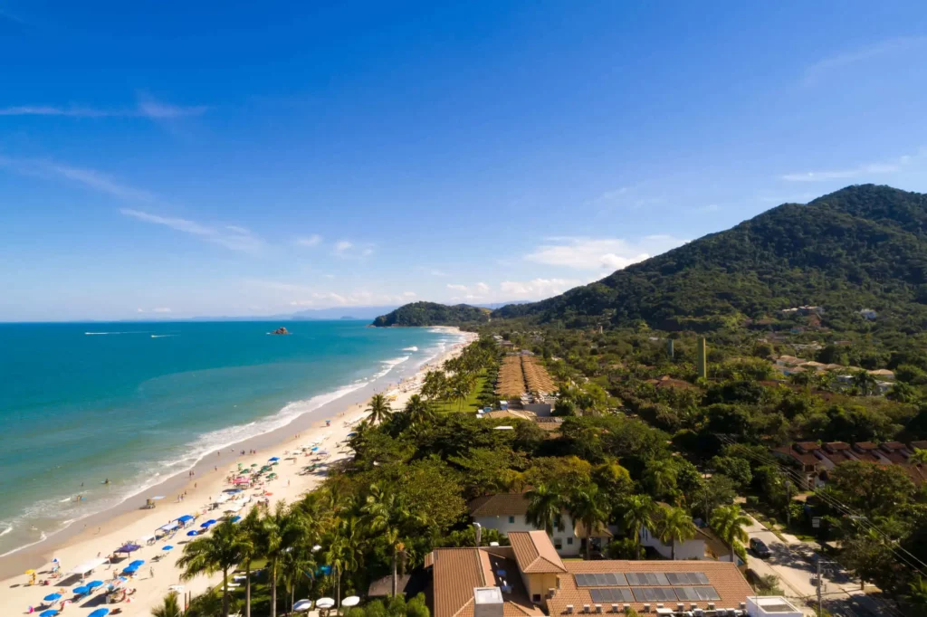 Imagem da vista aérea da Praia de Juquehy, em São Sebastião, mostra mar, faixa de areia e vegetação em um dia ensolarado