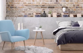 Foto de um quarto masculino com parede de tijolos, poltrona e livros.