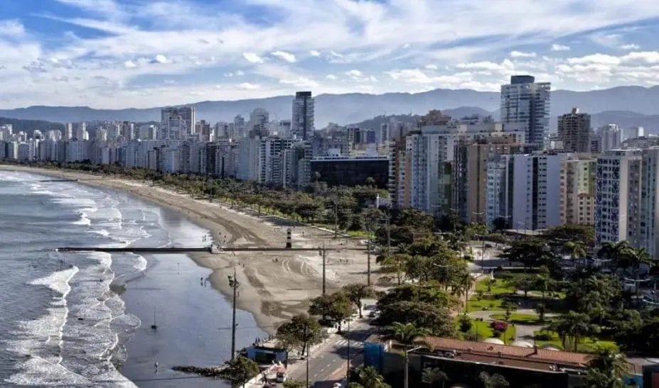 Imagem da vista aérea de Santos mostra prédios, vegetação, a orla e o mar em um ponto da cidade