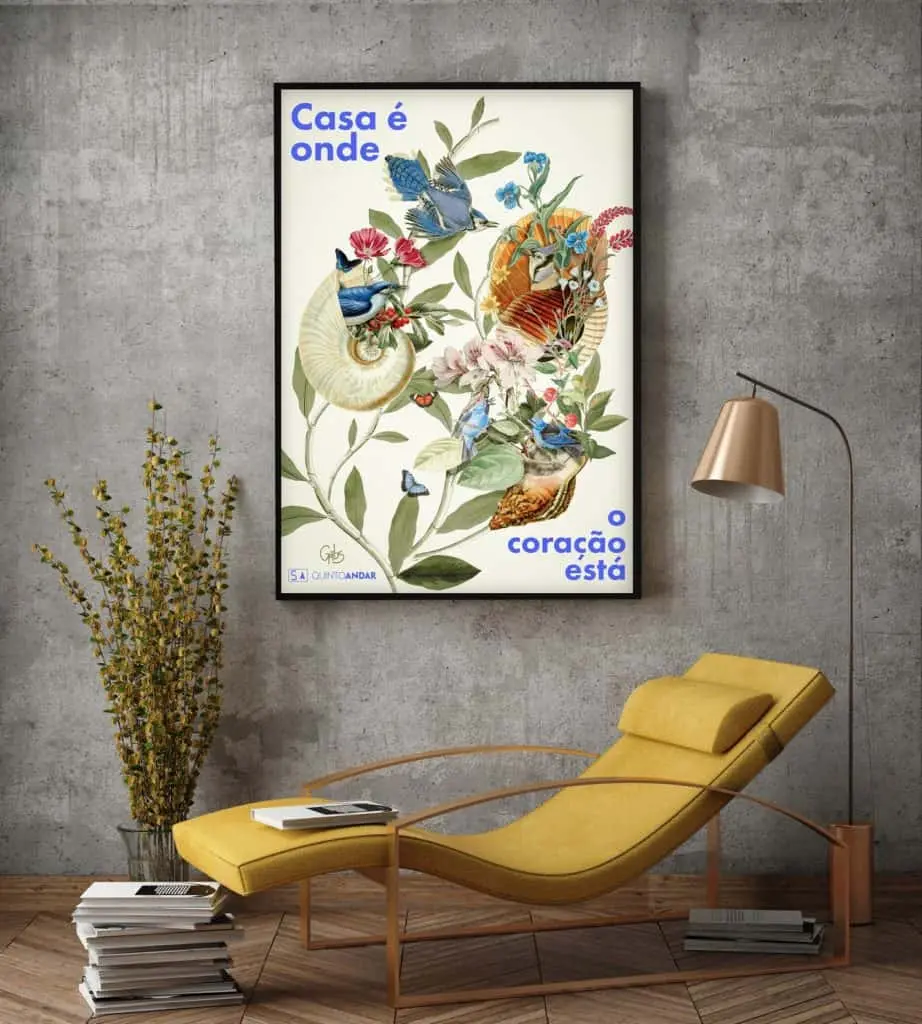 Uma sala moderna com parede cinza apresenta uma poltrona amarela, luminária, vaso com galhos e uma obra de arte emoldurada do QuintoAndar Colab, com pássaros, borboletas e plantas coloridas. A arte diz: Casa é onde o coração está.
