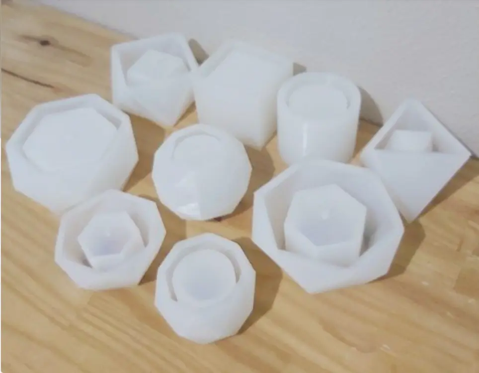 Um conjunto de moldes de silicone branco em vários formatos e tamanhos geométricos, perfeitos para criar vasos de cimento exclusivos, incluindo hexágonos, octógonos e círculos, colocados sobre uma superfície de madeira leve.