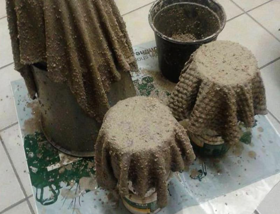 Três baldes cobertos com toalhas úmidas e drapeadas são cobertos com concreto molhado, criando um efeito texturizado e ondulado enquanto os vasos de cimento são colocados sobre um piso de ladrilho.