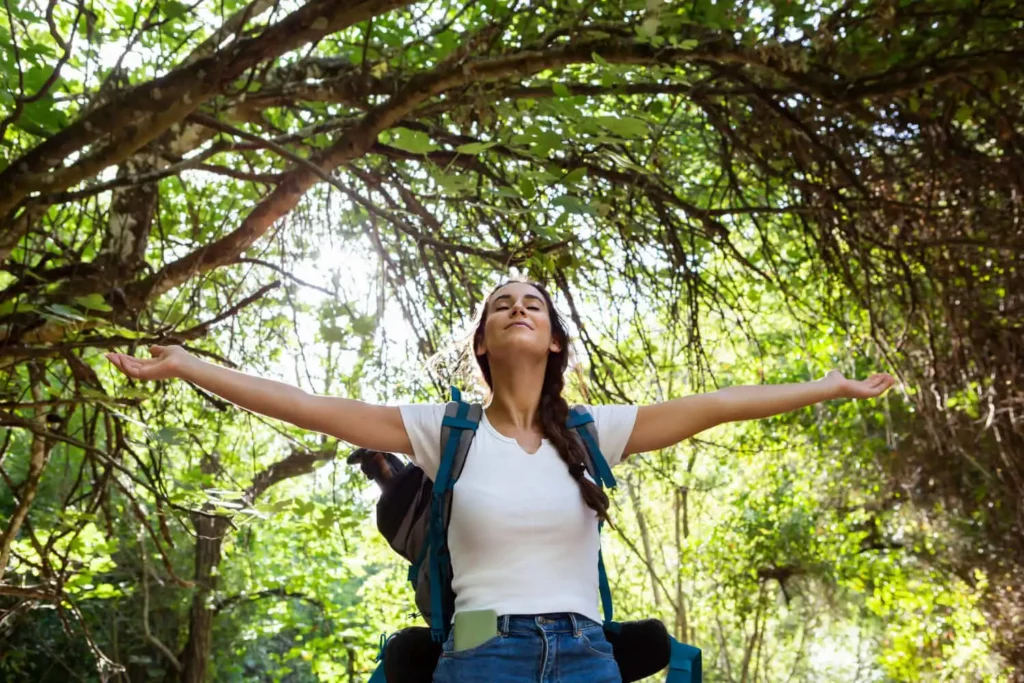 Imagem de uma mulher de braços abertos e com um semblante tranquilo em meio a natureza para ilustrar matéria sobre quais os benefícios de ir a parques