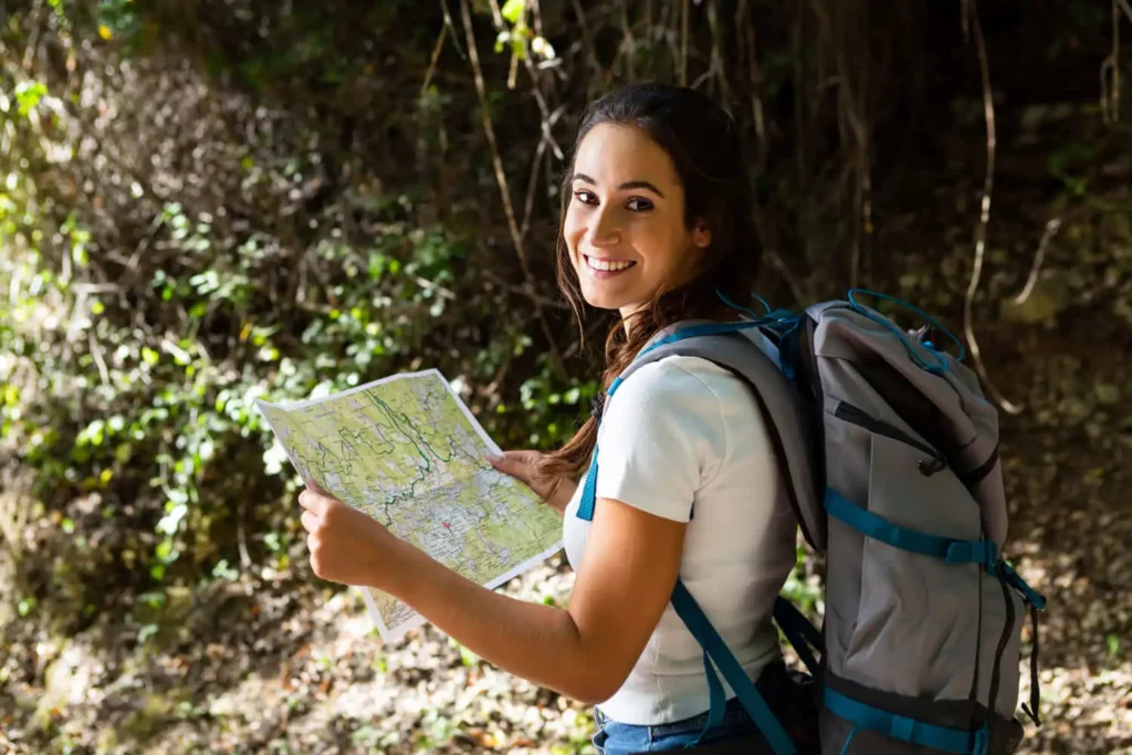 Imagem de uma mulher sorrindo e segurando o mapa em uma trilha na mata para ilustrar matéria sobre as cachoeiras disponíveis na cidade de São Paulo