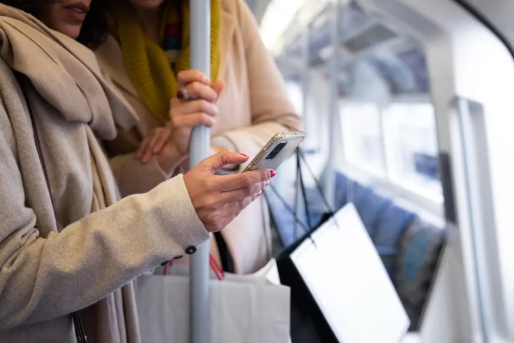Imagem da silhueta de duas mulheres olhando para a tela de um celular dentro de um trem para ilustrar matéria sobre como estão as obras da linha Prata, em São Paulo