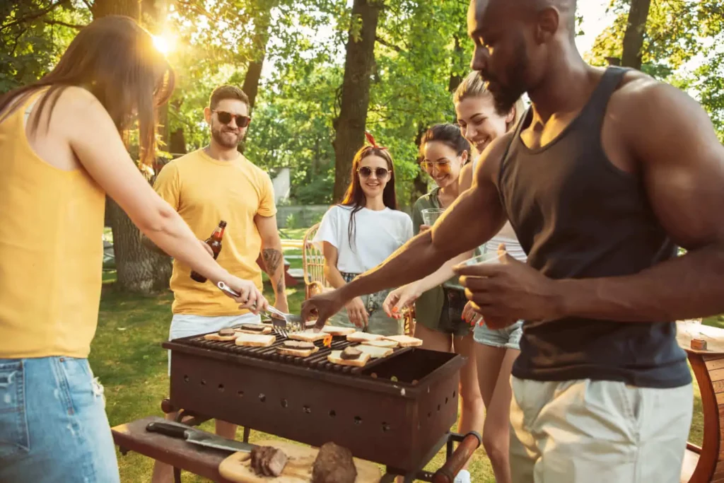Imagem de um grupo de amigos reunidos em torno de uma fogueira com carnes na brasa em meio a um parque para ilustrar matéria sobre parque na Zona Leste de São Paulo