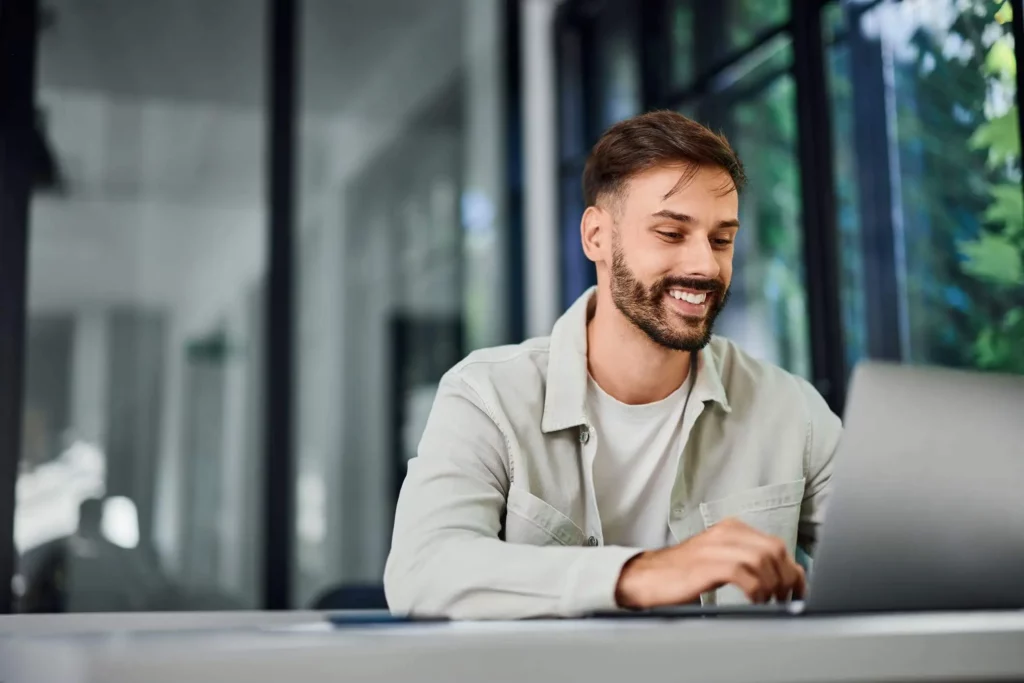 Imagem de um homem sorridente trabalhando no escritório mexendo no notebook para ilustrar matéria sobre Dimob, imobiliária