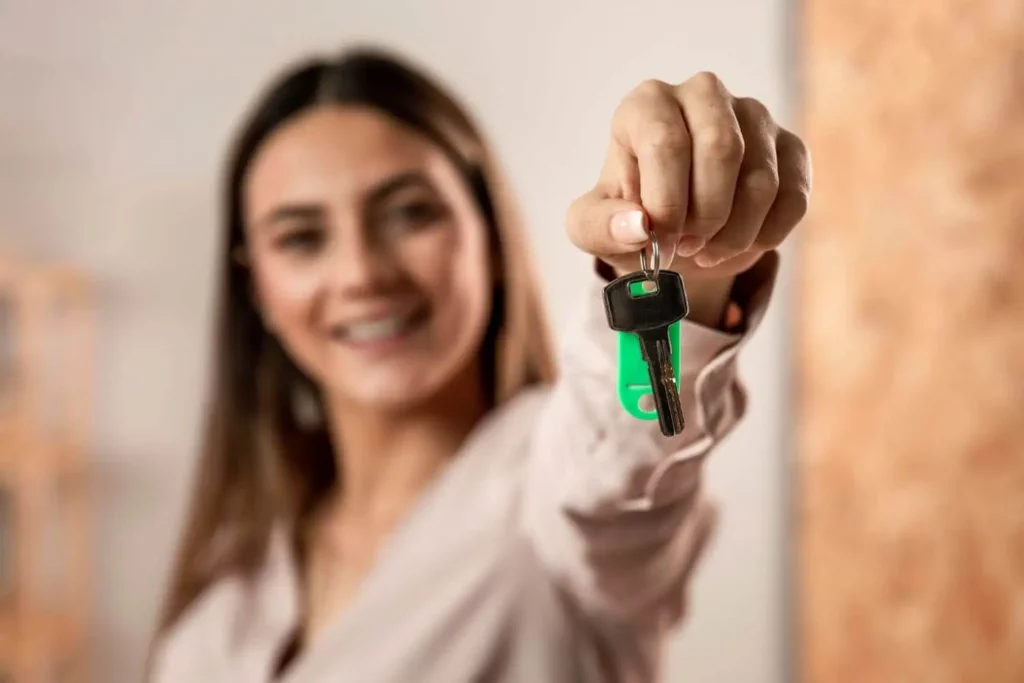 Imagem de uma mulher sorridente segurando uma chave para ilustrar matéria sobre se vale a pena vender imóvel e aplicar o dinheiro
