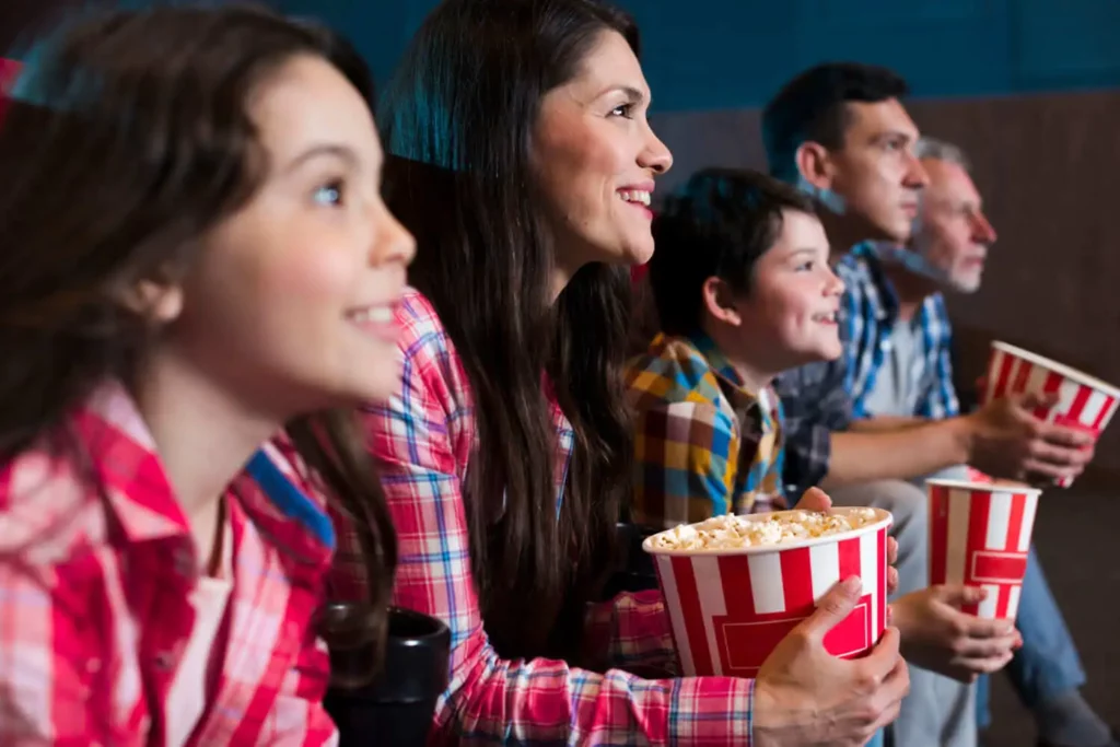 Imagem de uma família formada por dois homens, uma mulher e duas crianças concentradas assistindo a um filme com baldes de pipoca nas mãos para ilustrar matéria sobre cinemas de Uberlândia