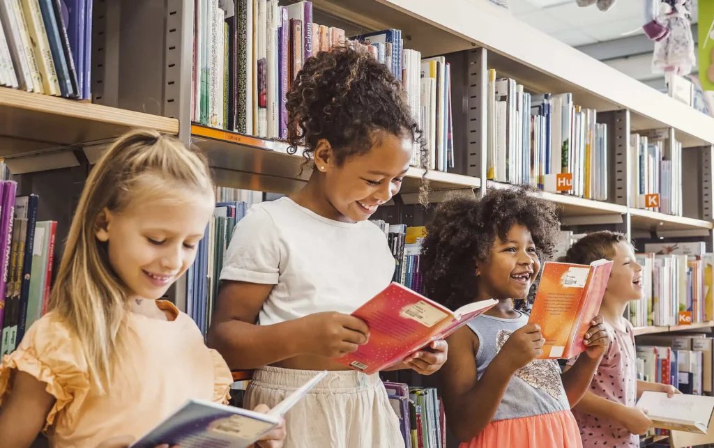 Imagem de quatro meninas encostadas em uma estante de livros lendo os livros escolhidos por elas em uma biblioteca para ilustrar matéria sobre as escolas particulares em Nilópolis - RJ