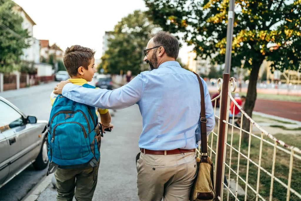Imagem de um pai colocando a mão nas costas do filho enquanto eles caminham em direção ao colégio para ilustrar matéria sobre as melhores escolas em Nilópolis, no Rio de Janeiro