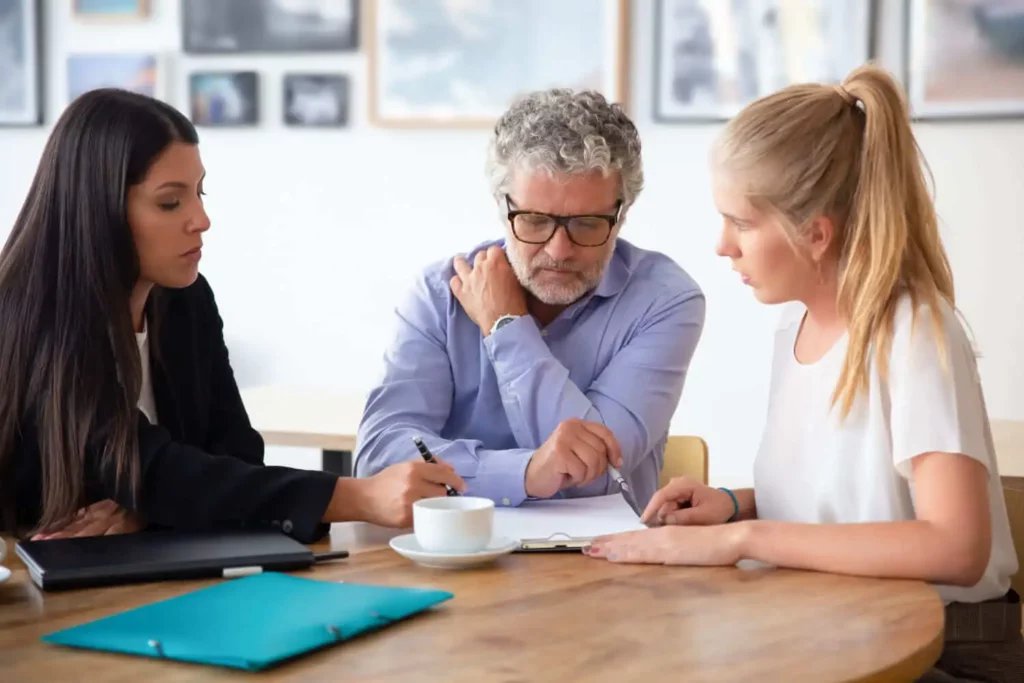 Imagem de um homem e duas mulheres sentados ao redor de uma mesa de madeiro analisando as informações contidas em um papel para ilustrar matéria sobre como expulsar herdeiro do imóvel