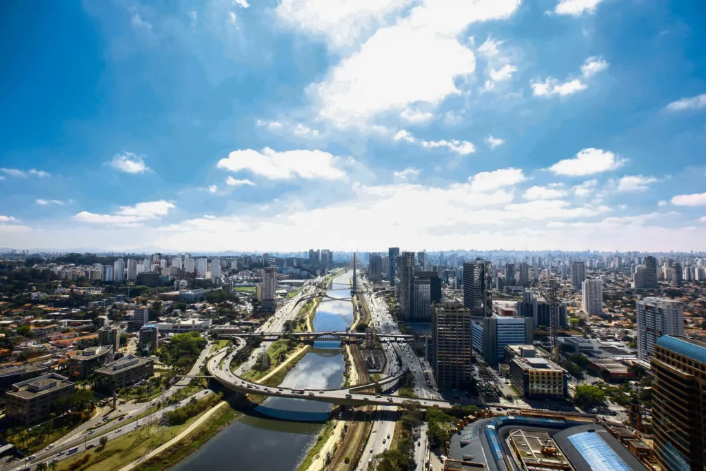 Imagem da vista aérea do rio Pinheiros mostra prédios, rio e avenidas em um dia de céu azul para ilustrar matéria sobre bairros em SP