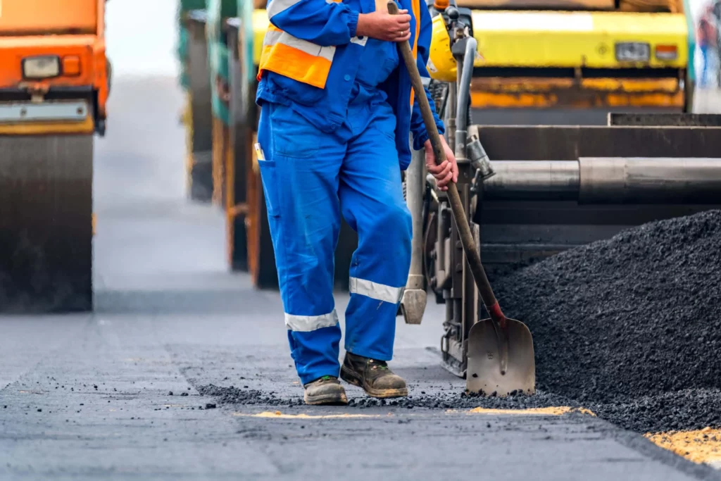 Imagem de um trabalhador e máquinas de asfaltamento fazendo a pavimentação de uma avenida para ilustrar matéria sobre como a contribuição predial funciona