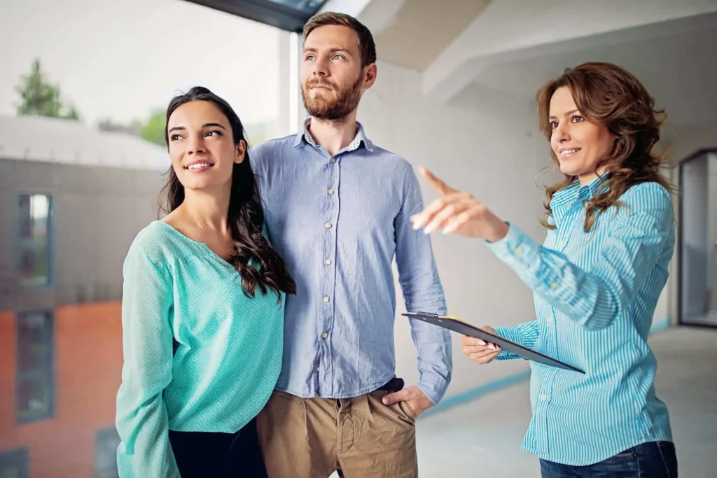 Imagem de um casal formado por um homem e uma mulher visitando um imóvel acompanhados de uma agente imobiliária para ilustrar matéria sobre bairro misto