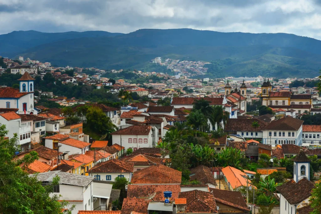 Imagem da paisagem urbana da cidade de Mariana vista de cima mostra casarões coloniais, vegetação e montanha ao fundo para ilustrar matéria sobre a cidade mais antiga de Minas Gerais