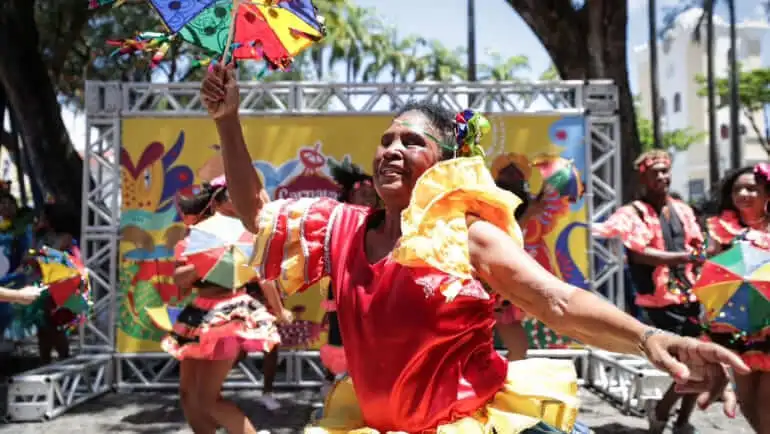 Imagem de uma mulher vestida com roupas características do frevo durante um bloco de carnaval em Recife para ilustrar matéria sobre como é o carnaval nas cidades grandes