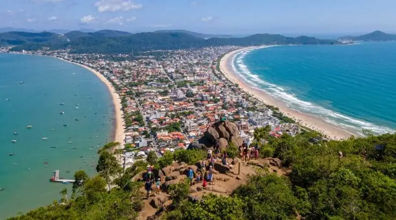 Imagem da vista aérea do Parque Natural Municipal Morro do Macaco mostra construções, vegetação, faixa de areia e mar para ilustrar matéria sobre parque em Santa Catarina