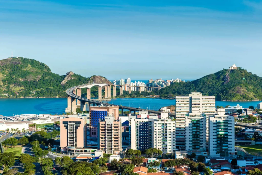 Imagem aérea de prédios residenciais cercado por mar e morros com árvore em Vitória, capital do Espírito Santo, para ilustrar matéria sobre os exemplos de cidades inteligentes no Brasil