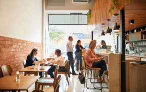 Imagem de uma cafeteria moderna com alguns clientes no caixa e outros sentados nas mesas consumindo café para ilustrar matéria sobre cafeterias em BH