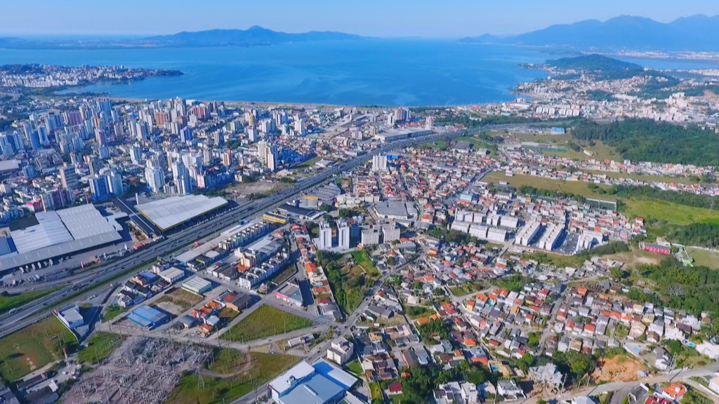 Imagem da vista aérea de São José (SC) mostra avenidas, prédios, casas, vegetação e mar ao fundo para ilustrar matéria sobre as cidades verticais no Brasil