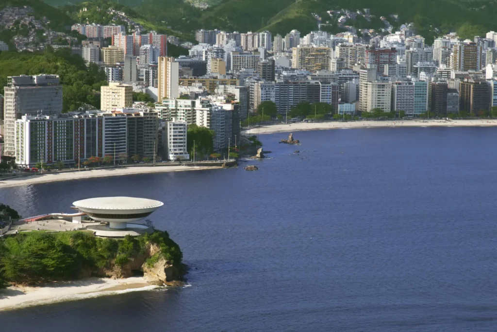 Imagem panorâmica com vista para o museu do Niemeyer, cercado de mar e próximo a prédios residências, em Niterói, para ilustrar matéria sobre as cidades verticalizadas do Brasil