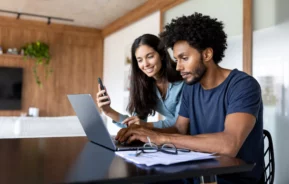 imagem que ilustra matéria sobre declarar imóvel quitado no IR 2025 mostra um casal sentado em frente ao computador