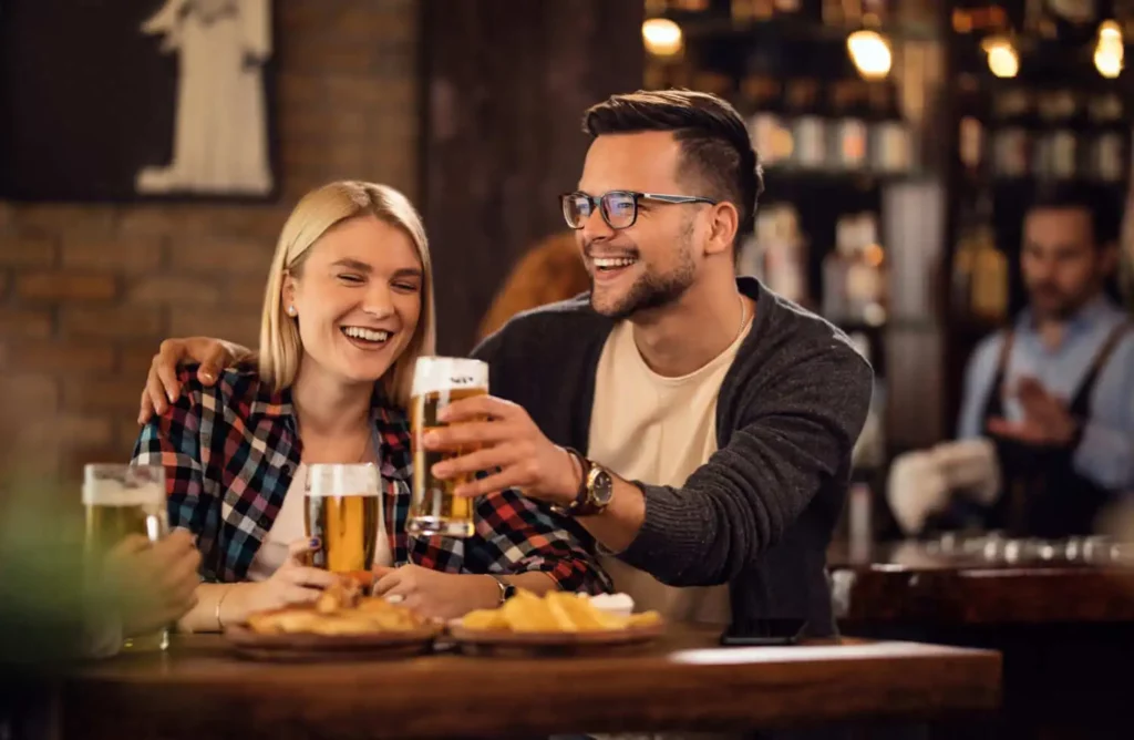 Imagem de um casal sorridente segurando um copo de cerveja em um bar para ilustrar matéria sobre os melhores bares e restaurantes de BH