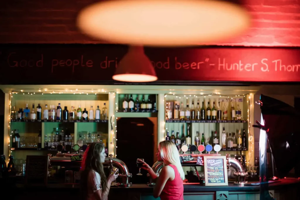Imagem panorâmica de duas mulheres jovens segurando taças de vinho em um bar