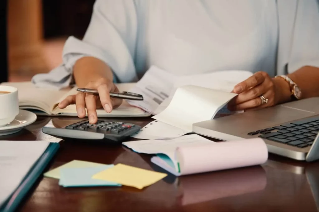 Imagem de uma mulher mexendo em uma calculadora próximo a uma mesa com papéis e um computador para ilustrar matéria sobre quais são os impostos sobre compra e venda de imóvel