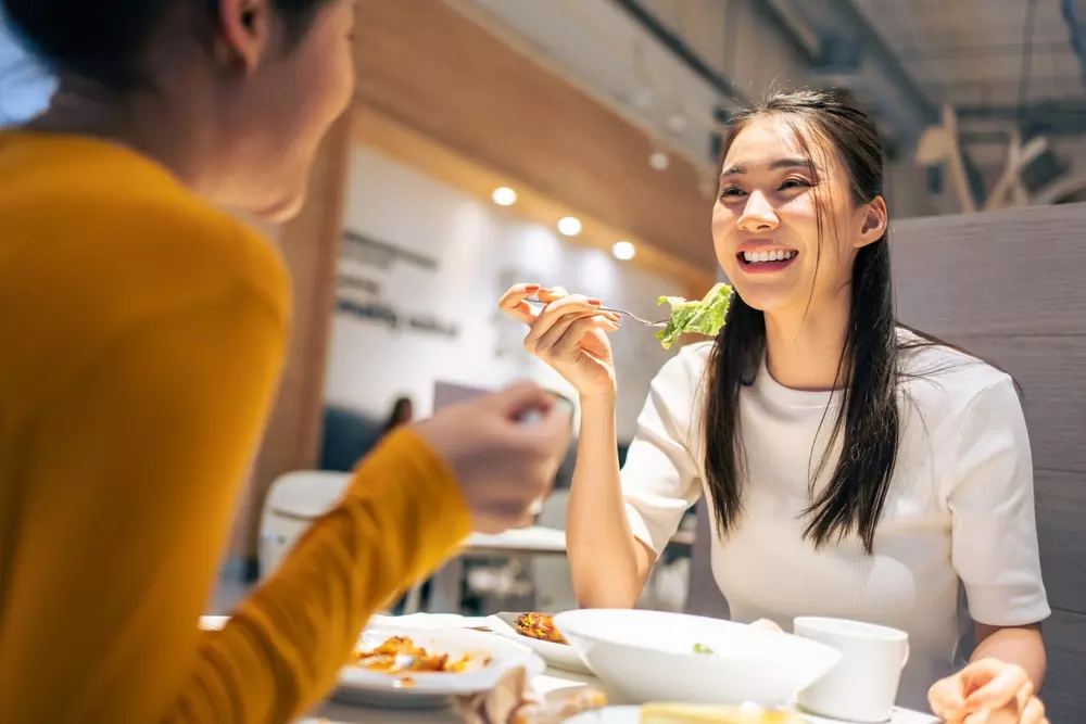 Duas amigas felizes almoçando em uma praça de alimentação de um shopping. Imagem ilustrando matéria que lista os principais shoppings em Niterói
