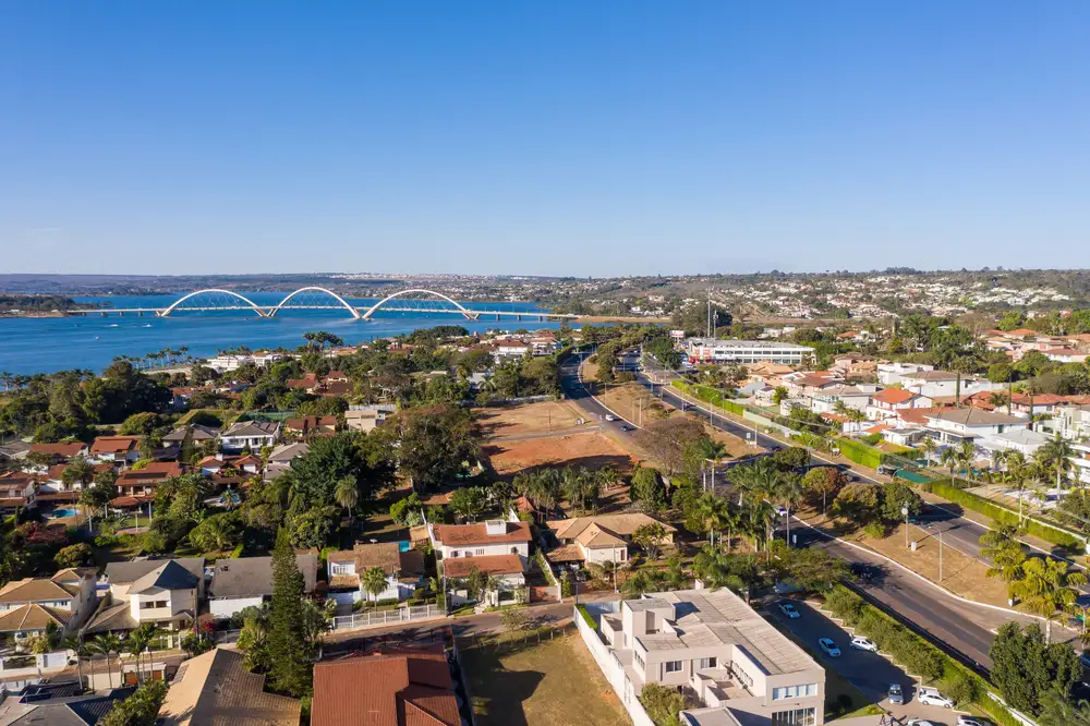 Imagem de vista aérea de uma região residencial do Lago Sul, em Brasília, com o Lago Paranoá e a Ponte JK ao fundo.