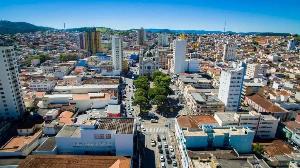 Imagem da vista aérea de Pouso Alegre, uma das cidades mais baratas para morar em Minas Gerais, mostra prédios, casas, avenidas e vegetação em um dia de céu azul