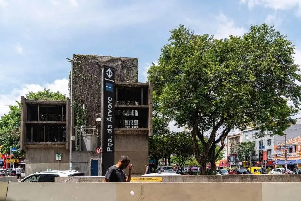 Imagem da entrada da estação Praça da Árvore, em São Paulo, mostra estrutura de concreto, placa com o nome da estação e uma árvore ao lado.