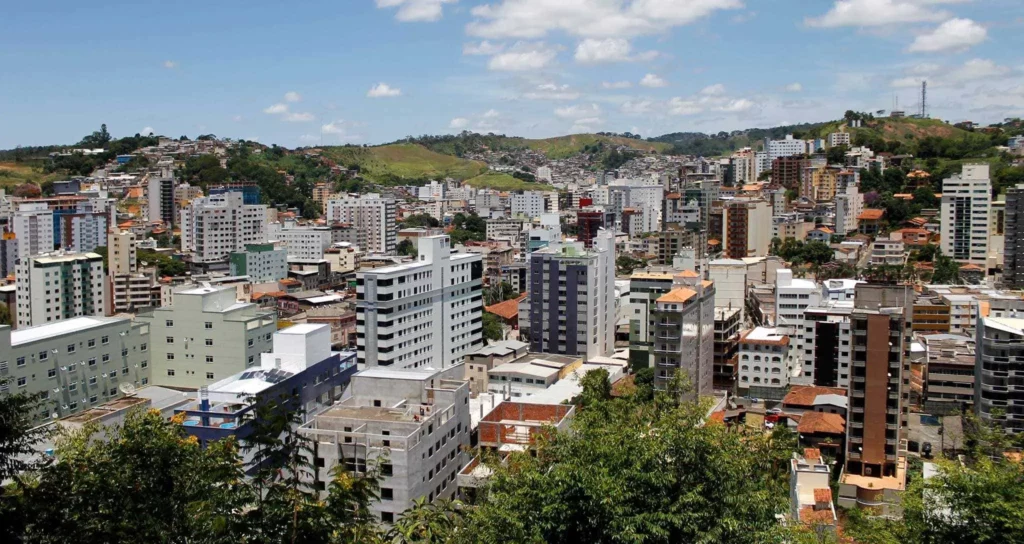 Imagem da vista aérea urbana de Viçosa, em Minas Gerais, mostra prédios e vegetação da cidade em um dia de céu azul